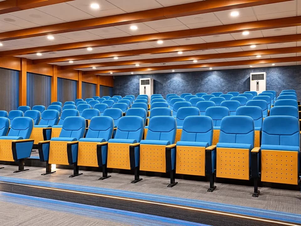 University auditorium with tiered blue seating and timber-beam ceiling.